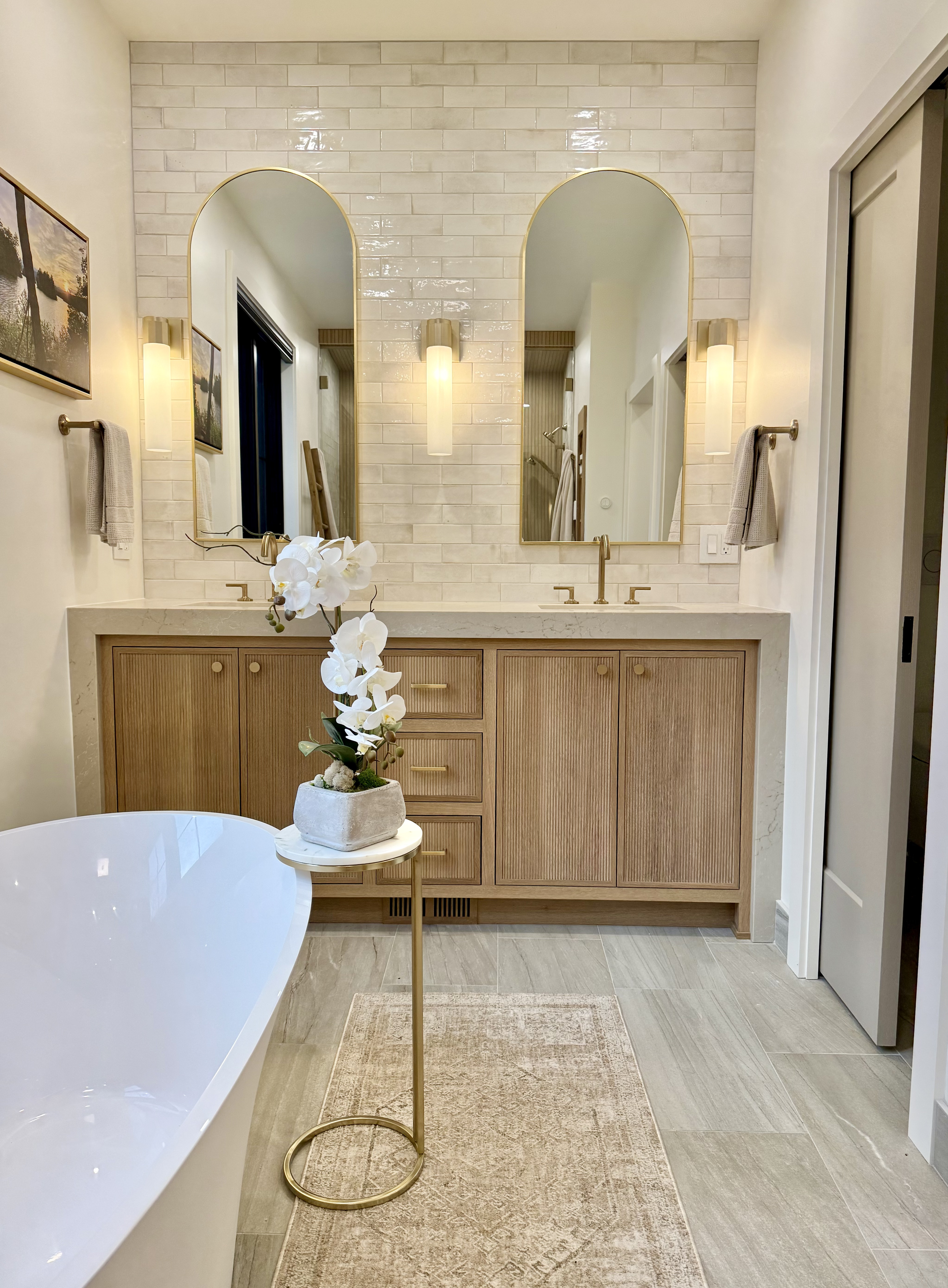 Double vanity with brass sconces and arched mirrors